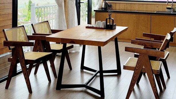 A modern dining area with a wooden table and chairs, large windows with curtains, and hanging pendant lights.