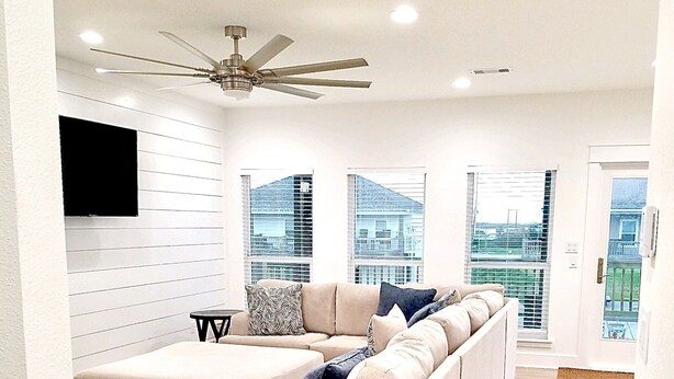 A modern living room with a sectional sofa, a small round table, and a ceiling fan. - Calypso Cove at Crystal Beach-Sleeps 12 (Bolivar Peninsula)