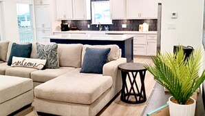 A modern living room with a beige sectional sofa, a small round side table, and a potted plant. - Calypso Cove at Crystal Beach-Sleeps 12 (Bolivar Peninsula)