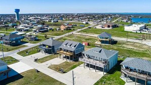An aerial view of a coastal town with a prominent water tower, residential buildings, and a marina. - Calypso Cove at Crystal Beach-Sleeps 12 (Bolivar Peninsula)