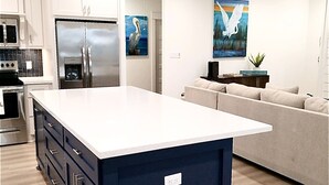 A modern kitchen with white cabinets, a stainless steel refrigerator, and a central island. - Calypso Cove at Crystal Beach-Sleeps 12 (Bolivar Peninsula)