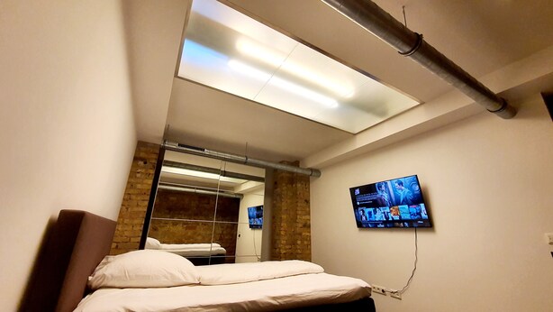 Habitación de hotel con cama, televisor montado en la pared y tragaluz sobre la cama.
