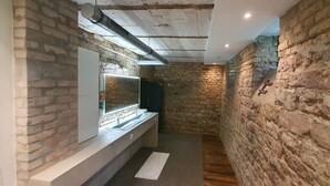 Un baño estrecho con pared de piedra, un lavabo moderno y un espejo.