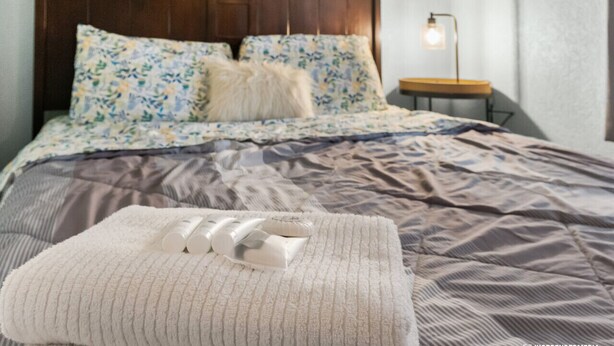 A neatly made bed with a floral-patterned duvet, a wooden headboard, and a bedside lamp. - Borealis Barnhouse - Slumber 7 (Anchorage)