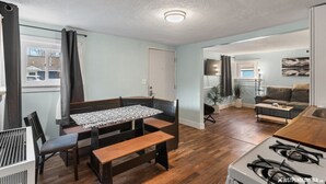 A compact living space with a kitchenette, a dining area with a bench, a sofa, and a TV. - Borealis Barnhouse - Slumber 7 (Anchorage)
