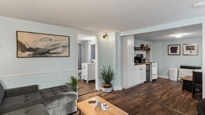 A modern living room with a grey sofa, a wooden coffee table, and a painting on the wall. - Borealis Barnhouse - Slumber 7 (Anchorage)