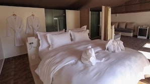 A hotel room with a large bed, two robes hanging on the wall, a sofa, and a small table. - The Farm Lodge & Spa (Marrakech)