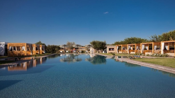 A pool area with wooden cabanas and a clear blue sky. - The Farm Lodge & Spa (Marrakech)