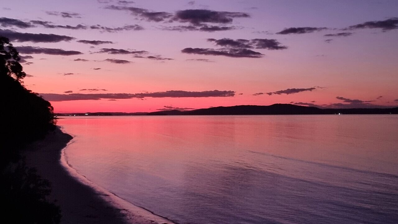 Una playa al atardecer con aguas tranquilas y cielo despejado.
