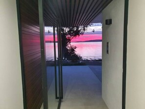 A corridor with a view of a sunset over a body of water, a tree, and a railing. - Vue One Nelson Bay Waterfront Luxury (Nelson Bay)
