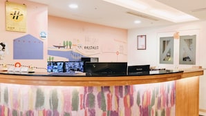 Ein Hotelrezeptionstresen mit einem farbenfrohen, abstrakten Wandbild, einem ViewSonic-Monitor und einem gerahmten Zertifikat an der Wand.