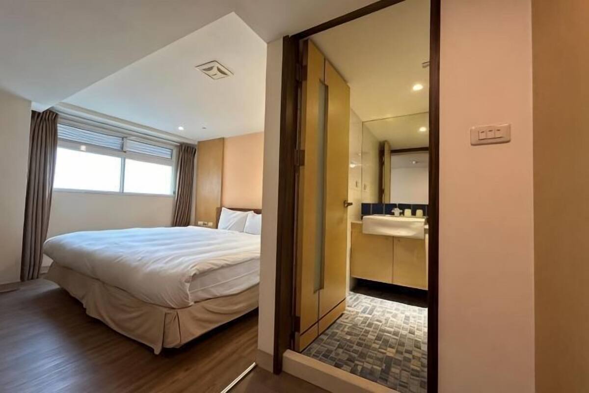 A hotel room with a bed, a bathroom with a sink, and a view of the outside.