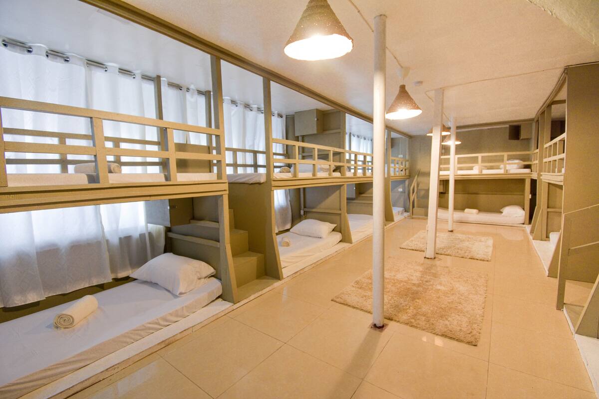 Um quarto tipo dormitório com beliches, uma escada e um luminário.