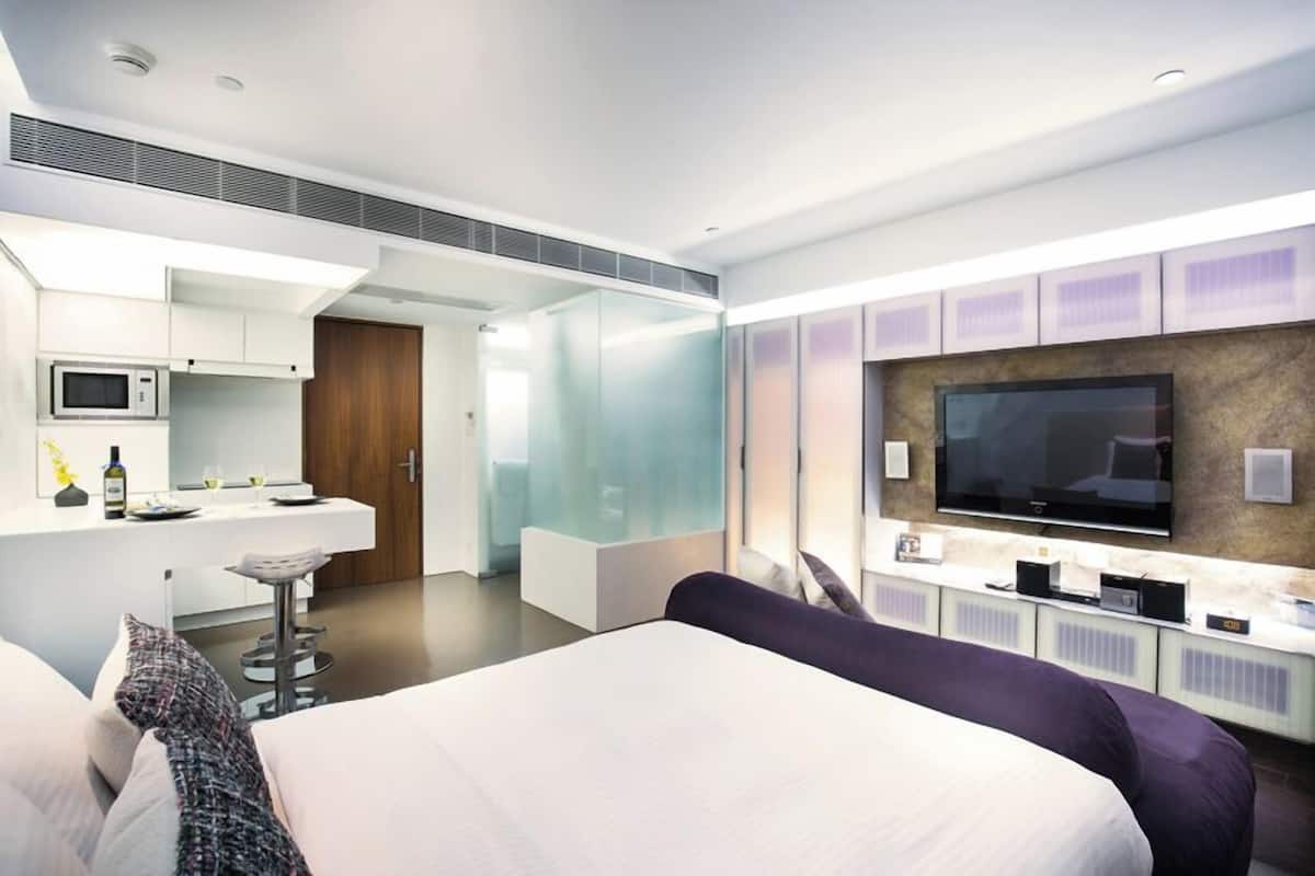 A modern hotel room with a large bed, a TV, a minibar, and a separate dining area.