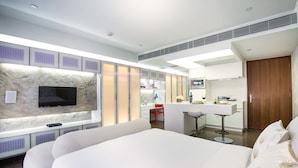 A modern hotel room with a large bed, a TV mounted on a textured wall, a kitchen area with a bar, and a wooden door. - V Wanchai (Hong Kong)