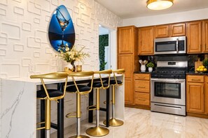 A kitchen with wooden cabinets, stainless steel appliances, and a bar area with gold bar stools.