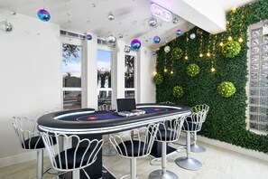 Una mesa de juegos con sillas, un letrero de neón y una pared verde con detalles decorativos.