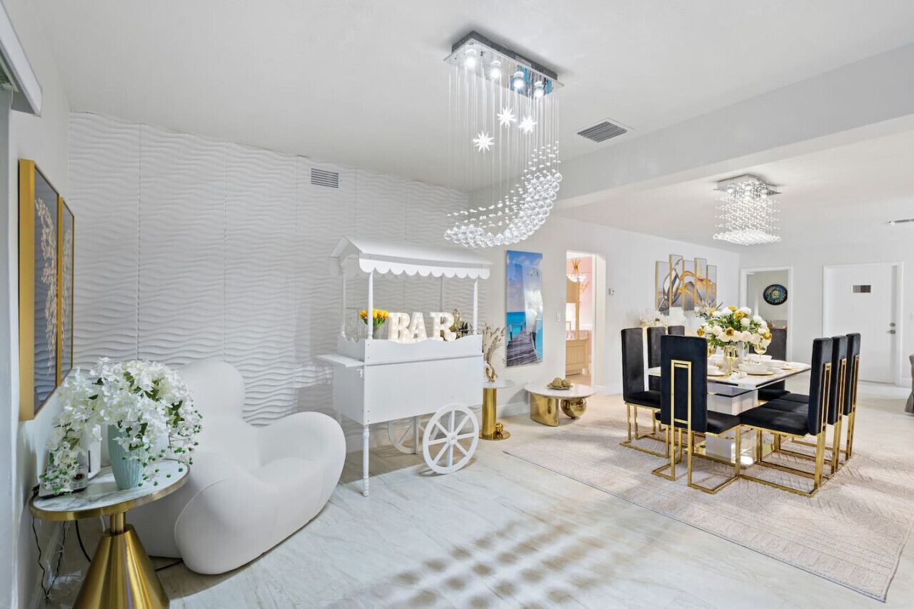 A modern dining area with a white bar cart, gold accents, and a chandelier.