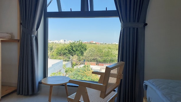 A room with a large window, a wooden chair, and a small table. - Windy Homestay Phan Thiet (Phu Thuy)