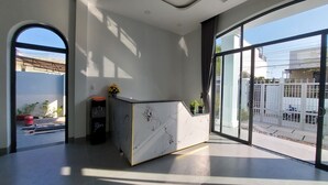 A modern reception area with a marble counter, large windows offering views of the street, and a water dispenser. - Windy Homestay Phan Thiet (Phu Thuy)