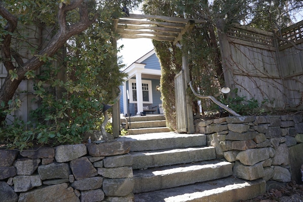 A stone staircase leading to a wooden pergola with a view of a house.