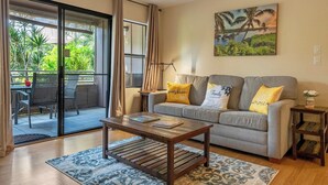 A living room with a sofa, a coffee table, and a painting on the wall. - Perch - Maui condo: Pool, beach access, daily tranquility on lanai – an indulgent escape. (kihei)