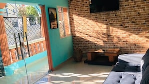 Une pièce avec un mur en briques, un canapé, un téléviseur fixé au mur et une porte en verre avec un portail en métal.