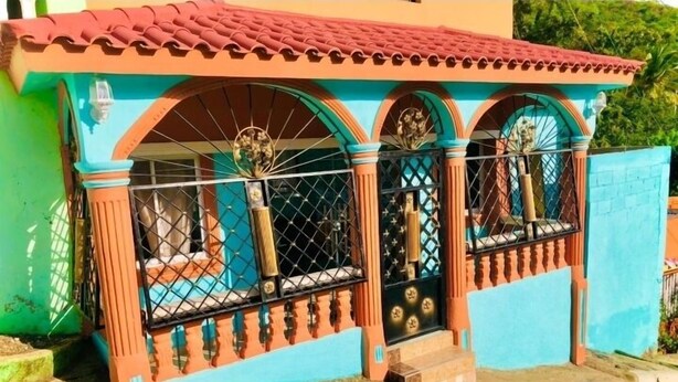 Un bâtiment doté d’un toit recouvert de tuiles rouges, de murs bleus et d’une entrée fermée par un portail agrémenté d’arches décoratives.