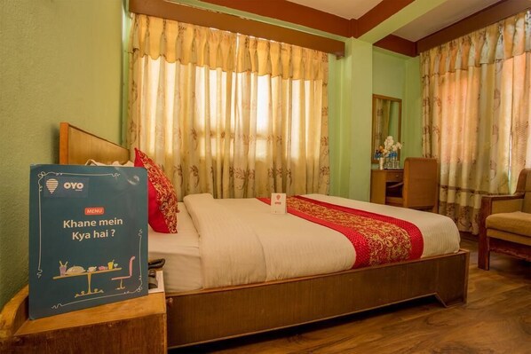 A hotel room with a bed, a wooden nightstand, a chair, and a desk with a mirror. - Hotel Green Orchid pvt ltd (Kathmandu)