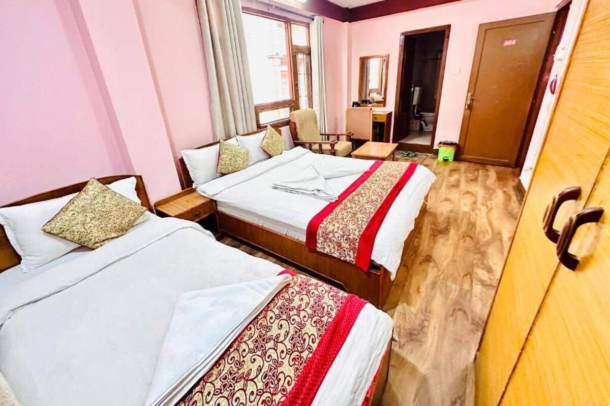 A hotel room with two beds, a desk, a chair, a wardrobe, and a mirror.