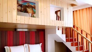 Een hotelkamer met een bed, een schilderij, een trap en uitzicht op buiten.