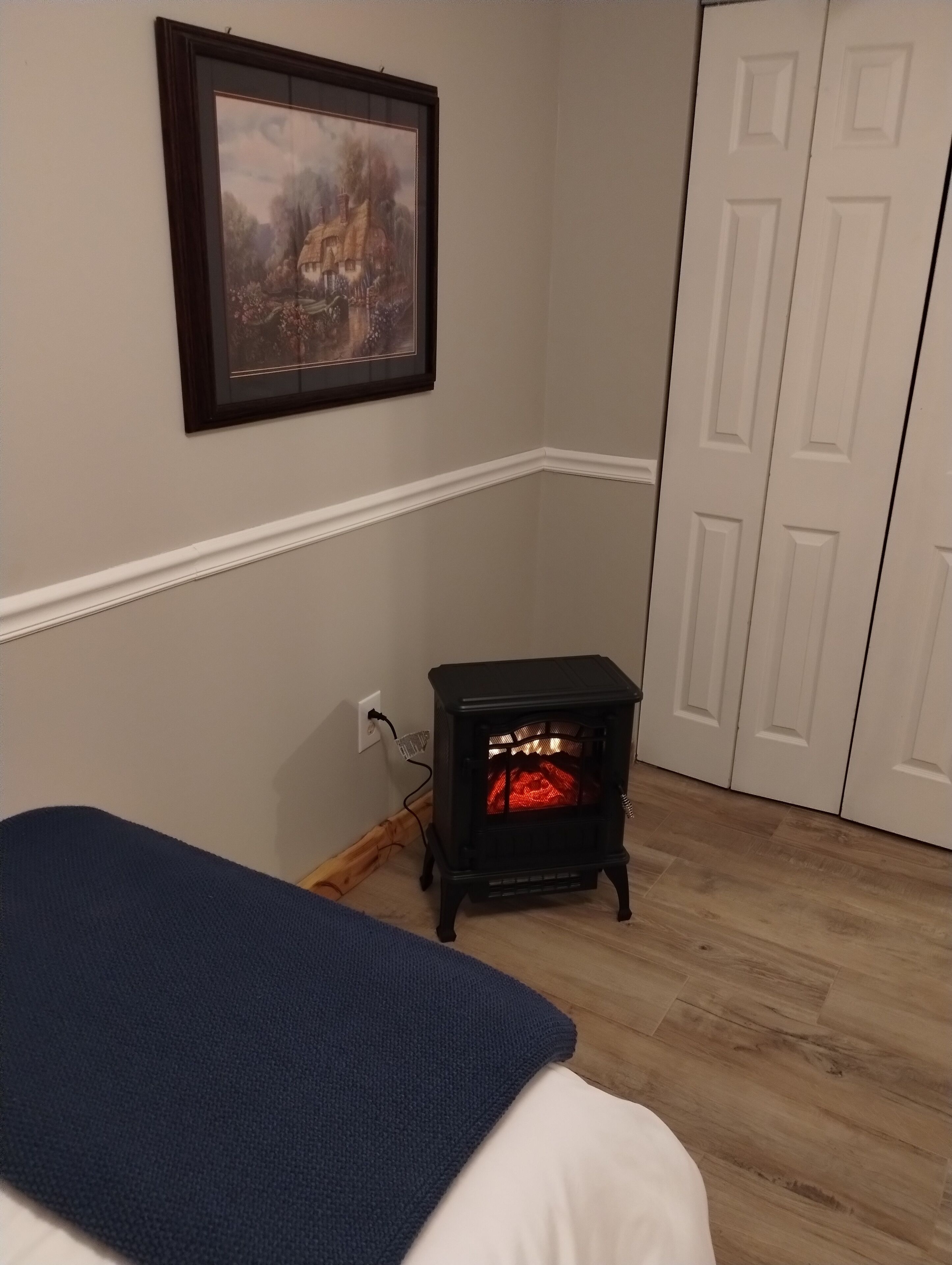 A room with a bed, a small heater, a framed picture on the wall, and a door.