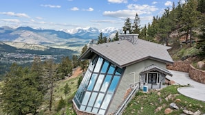 Una casa moderna con amplios ventanales de vidrio, fachada de piedra y vistas a montañas.