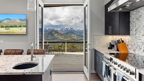 Una cocina moderna con una isla grande, horno y vistas a montañas a través de una puerta abierta.
