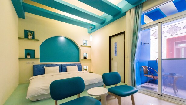 Een moderne hotelkamer met een bed, twee stoelen, een kleine tafel en een balkon met een stoel.