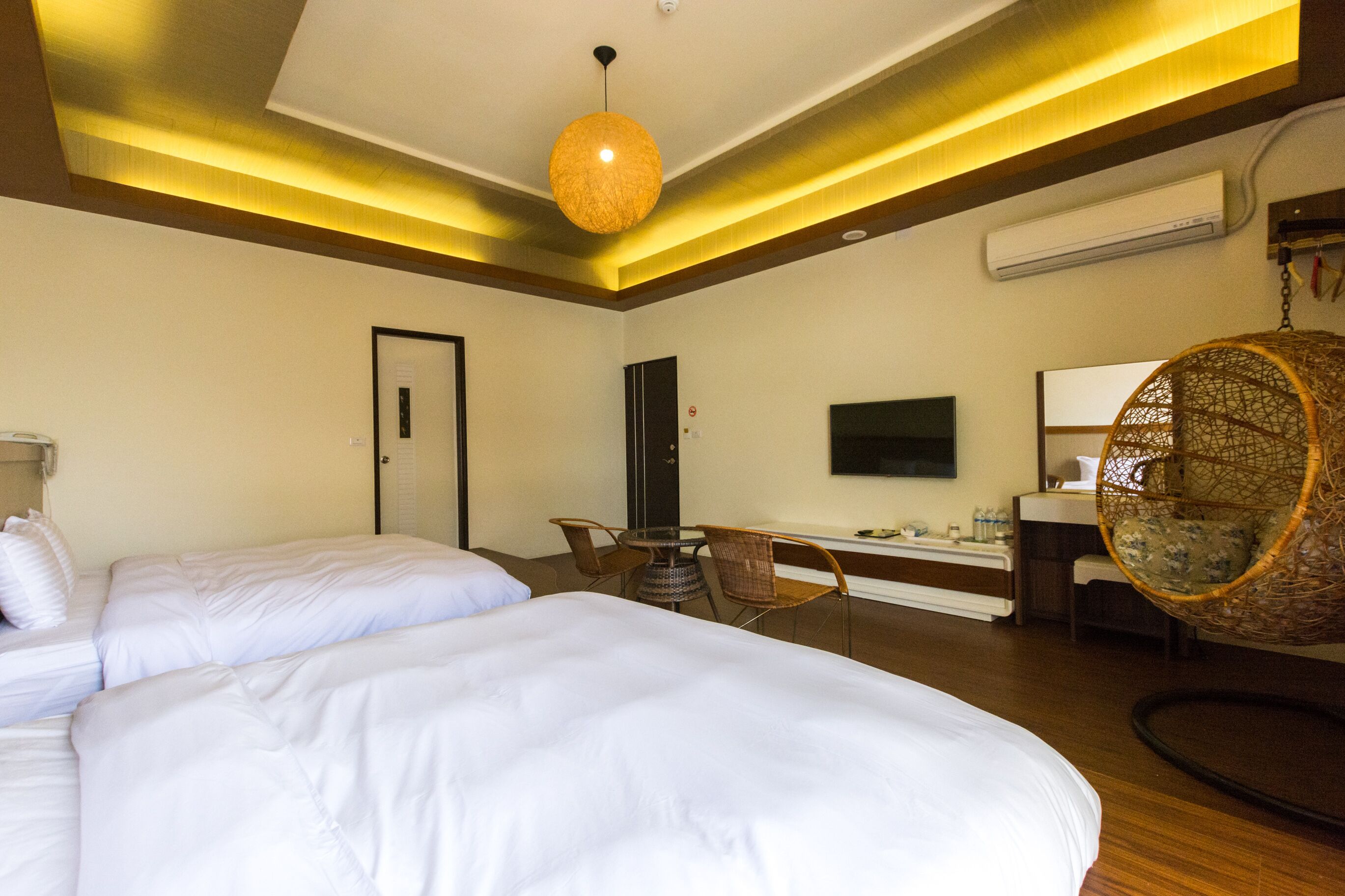 A hotel room with two beds, a desk, a chair, a hanging chair, and a television.