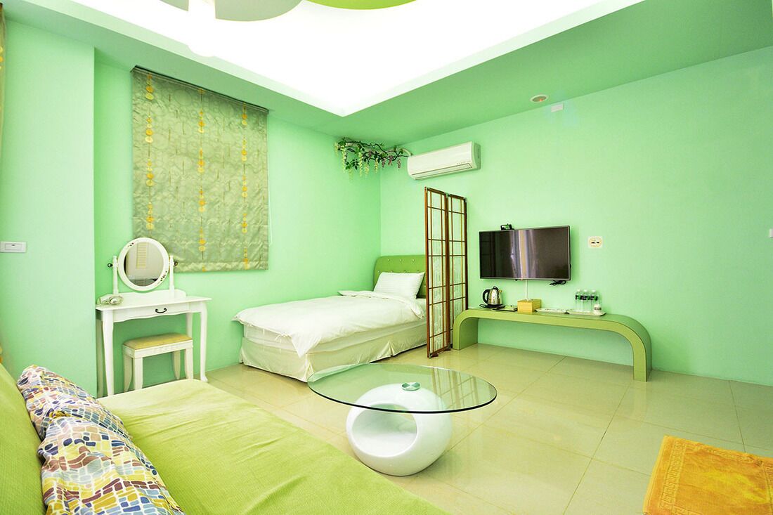 A room with a bed, a small desk with a mirror, a glass table, a TV, and an air conditioning unit.