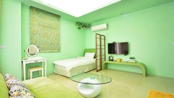 A room with a bed, a small desk with a mirror, a glass table, a TV, and an air conditioning unit.