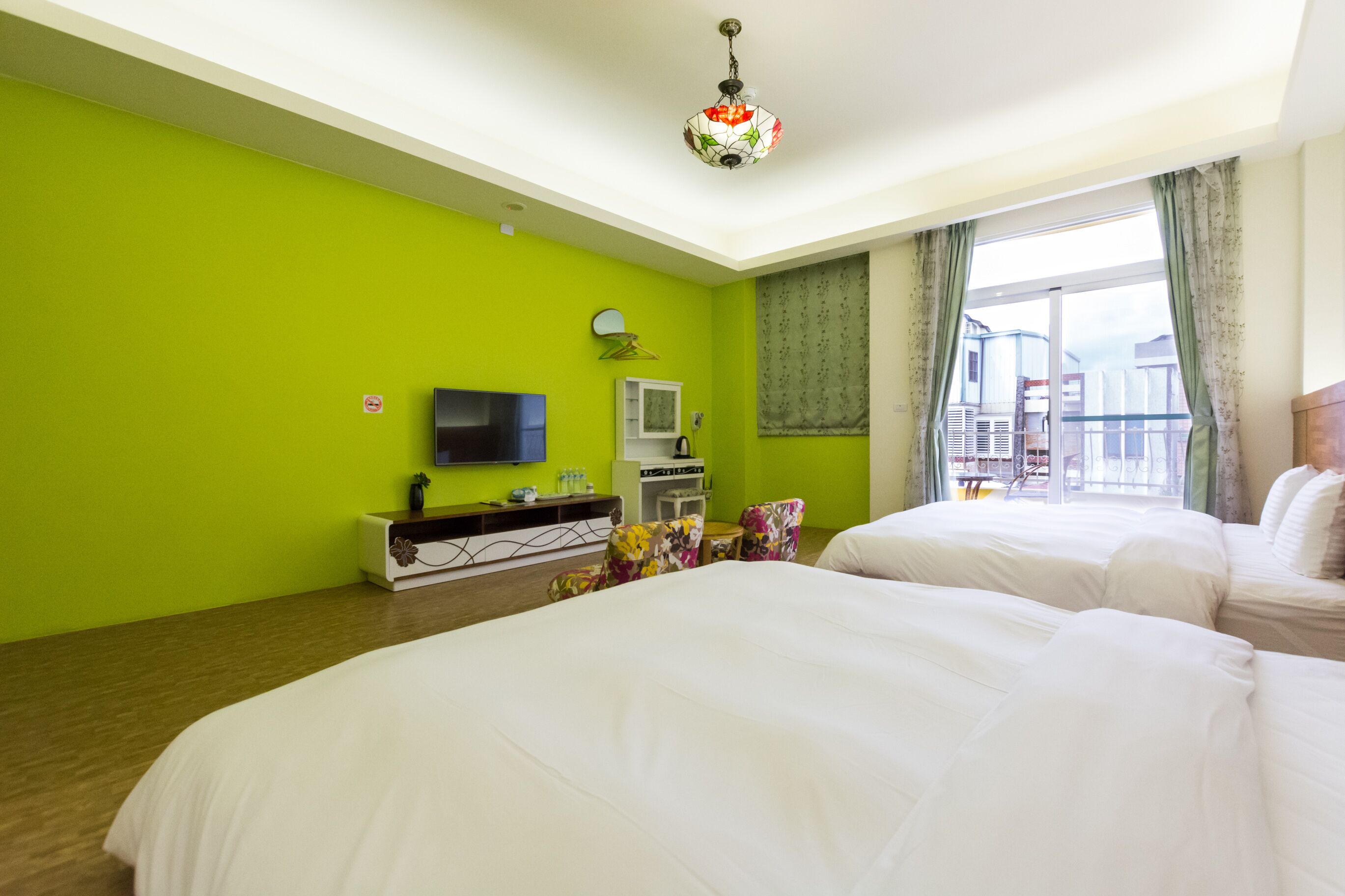 A hotel room with two beds, a TV, a minibar, and a balcony with a view.
