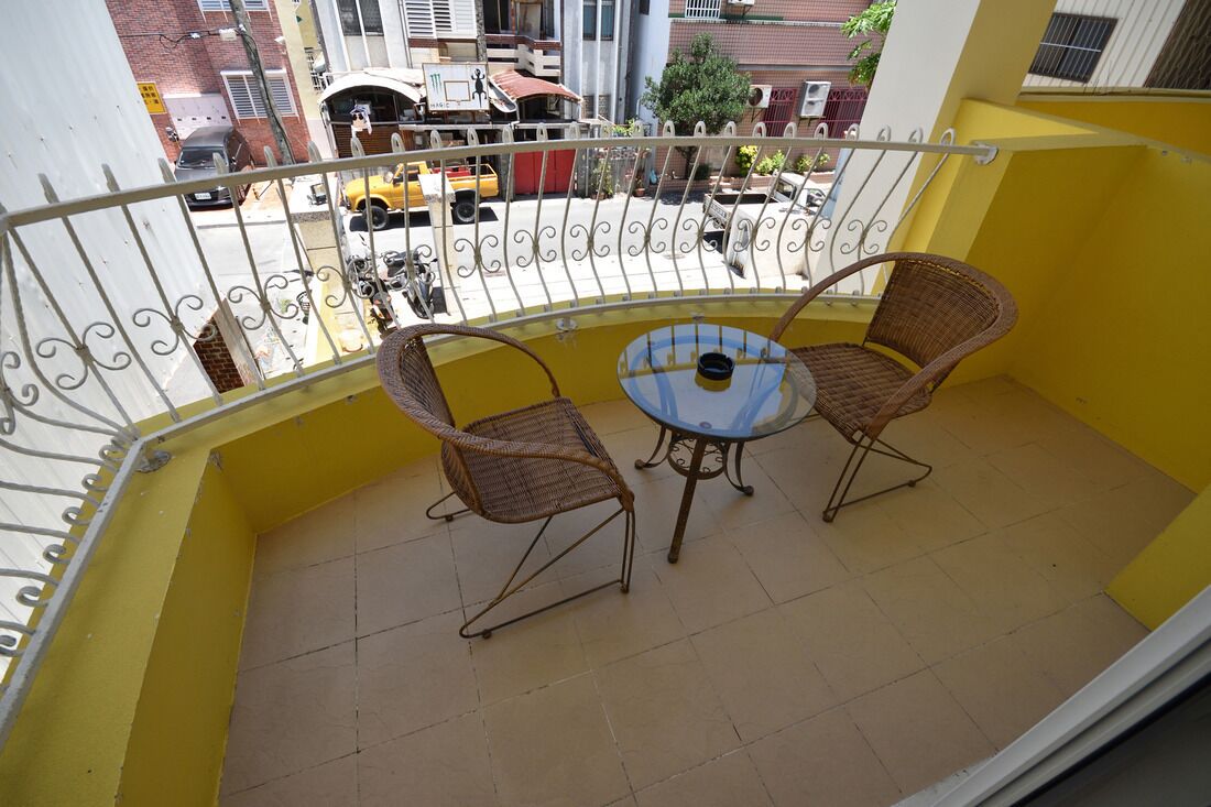 A balcony with yellow walls, a metal railing, two wicker chairs, and a small round table.