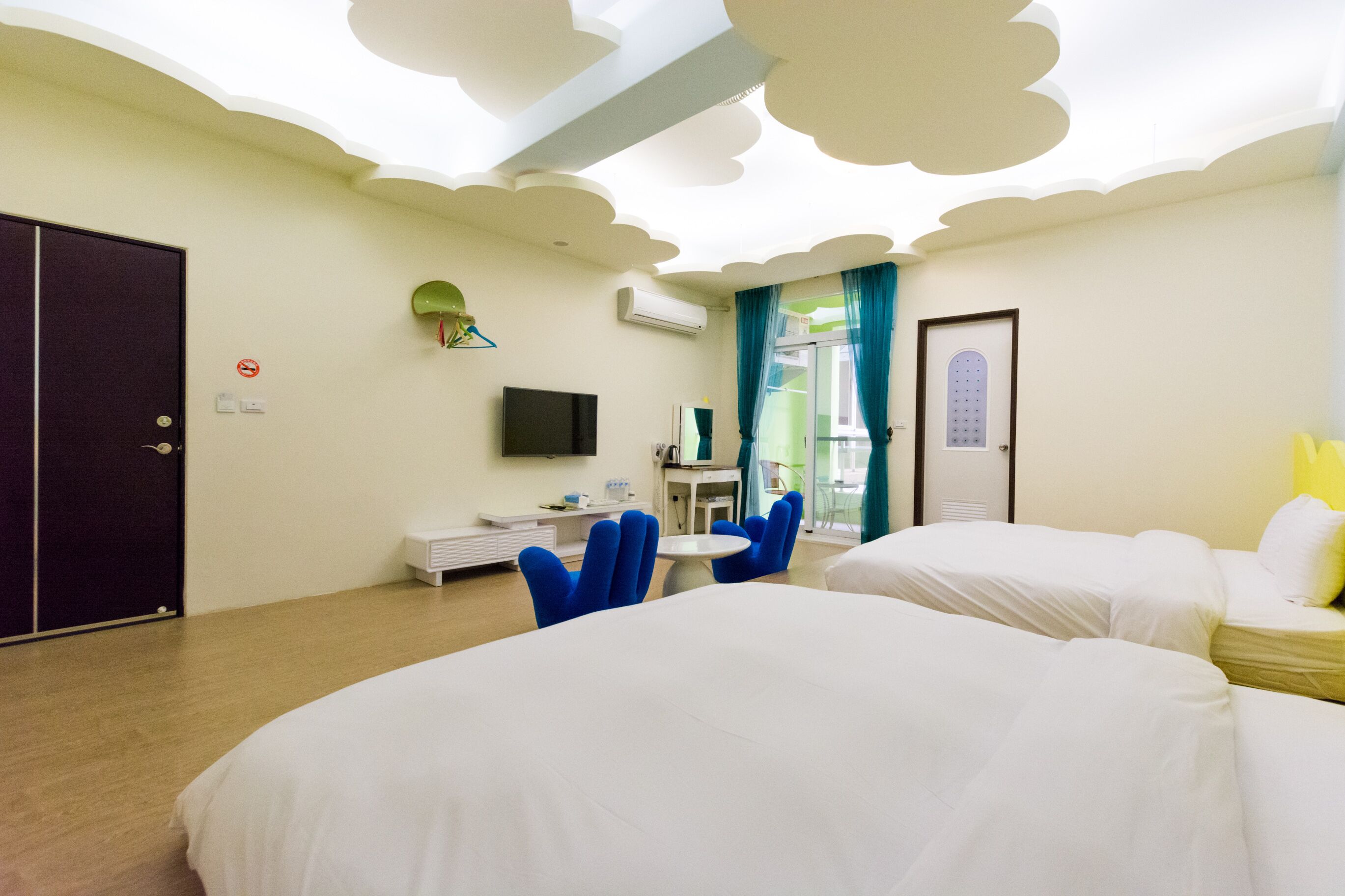 A hotel room with two beds, a desk, a chair, a TV, and a door.