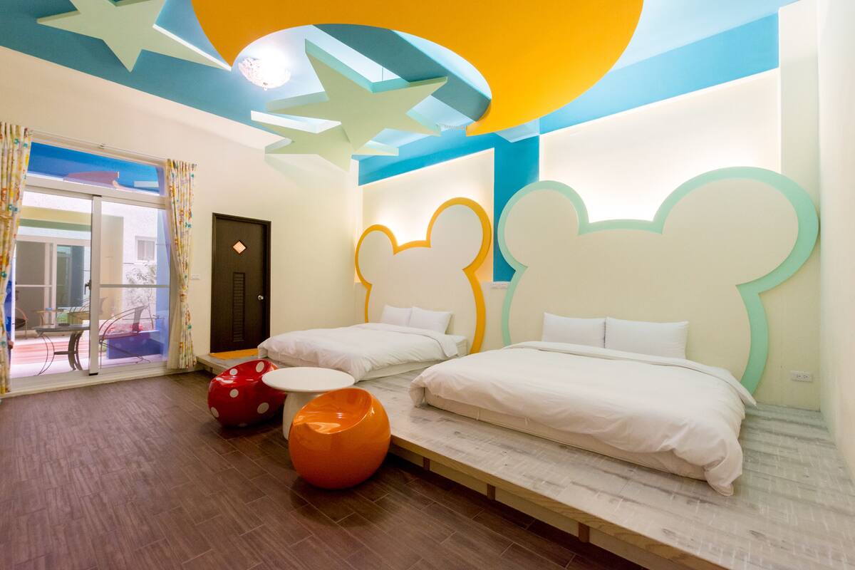 Quarto de hotel com duas camas, janela com cortinas, porta e vista para o exterior.