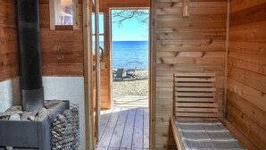 A wooden cabin with a bench, a fireplace, and a view of the sea. - Sisu Shores: Lakefront Home with Private Beach and Wood Burning Sauna (Duluth)