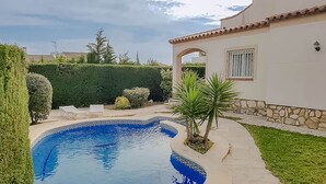 Una piscina con un diseño geométrico de azulejos, rodeada de un césped cuidado y un muro de piedra.