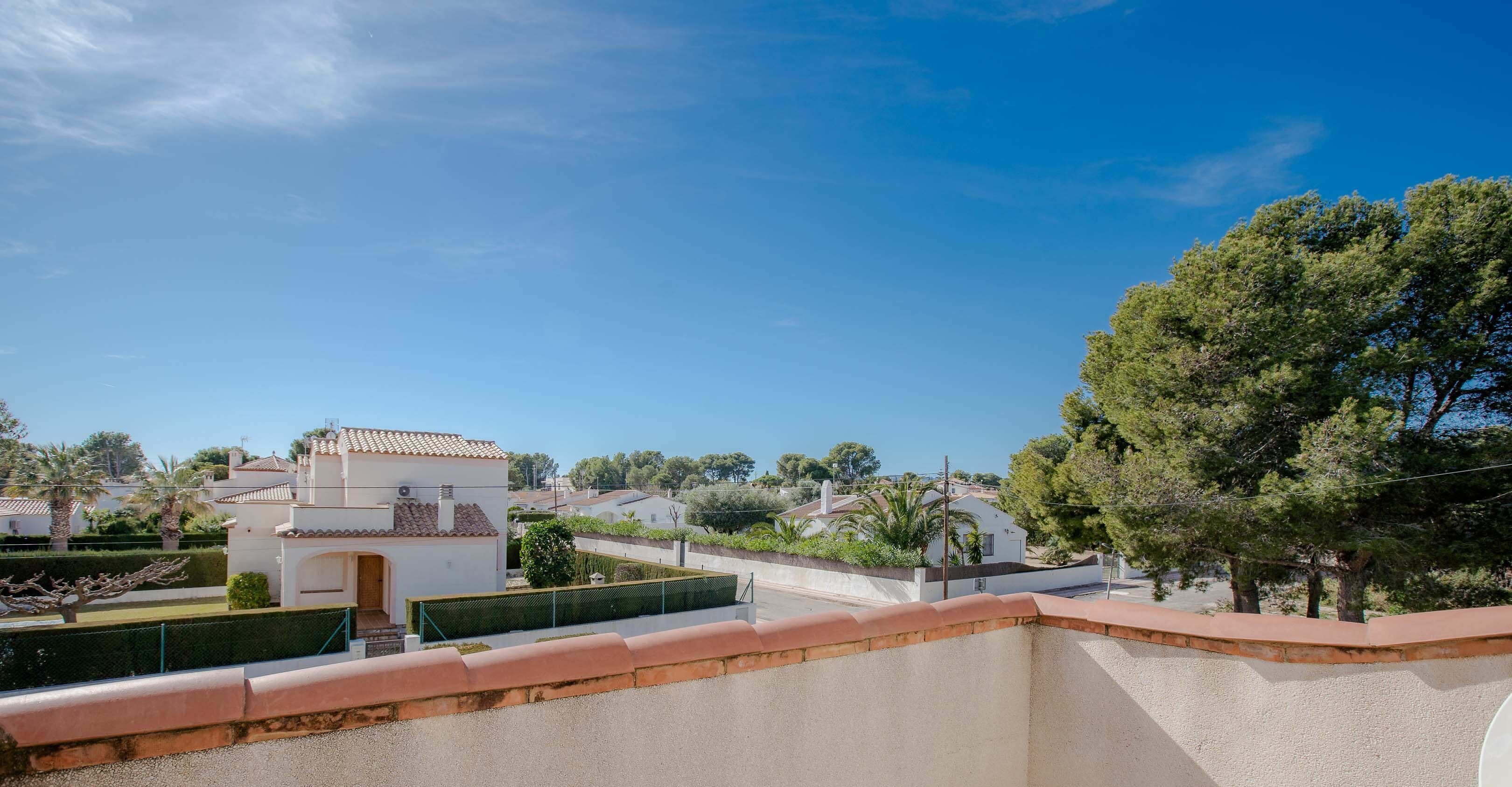 Un quartier résidentiel avec un immeuble blanc doté d’un toit en tuiles, entouré de verdure et d’autres maisons.