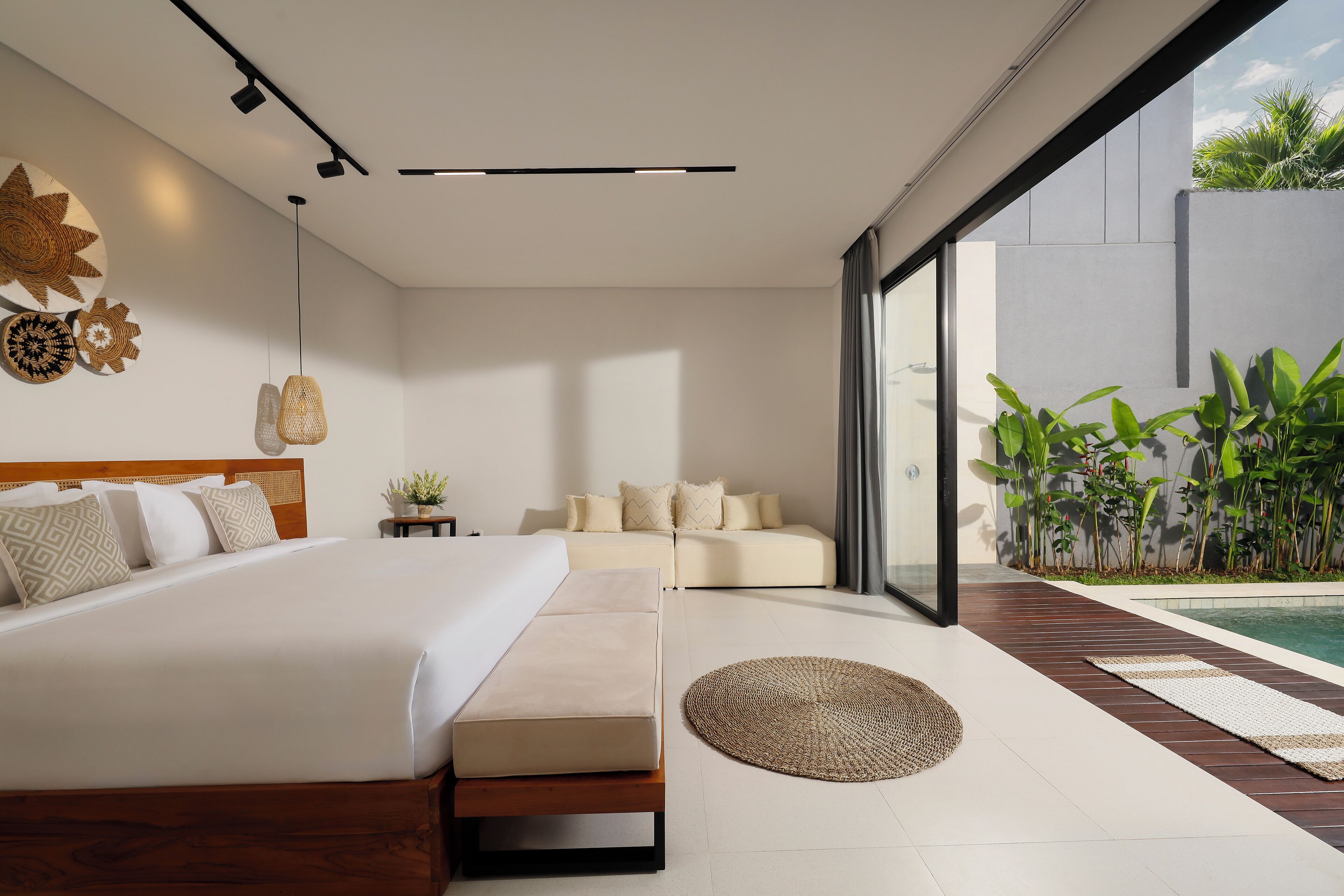 A modern bedroom with a large bed, a sofa, and a view of a swimming pool.
