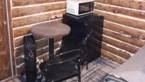 A corner room with a wooden log wall, a small black table with a white microwave on top, a black chair, and a black computer. - cozy cabin (Copper Center)