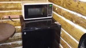 A compact kitchen area with a microwave on top of a black appliance, possibly a mini-fridge, against a wooden wall. - cozy cabin (Copper Center)