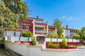A multi-story residential building with a red and white facade, balconies, and a gated entrance. - Apartment Ayni With Private Pool (Umag)