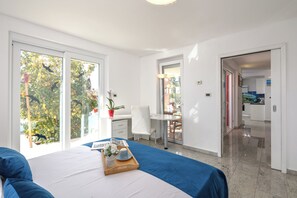 A hotel room with a bed, a desk, a chair, a dining table, and a view of the outdoors. - Apartment Ayni With Private Pool (Umag)
